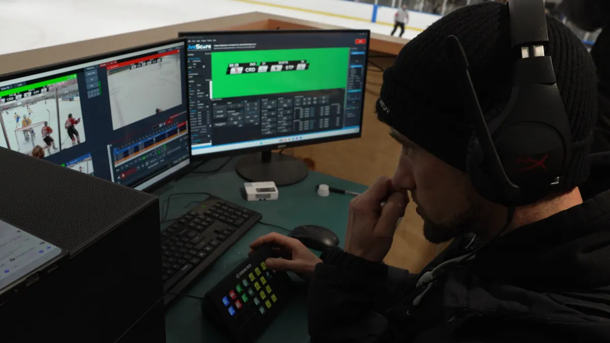 Directing the ice hockey stream in vMix, with a Stream Deck under hand and the rink beyond the monitors