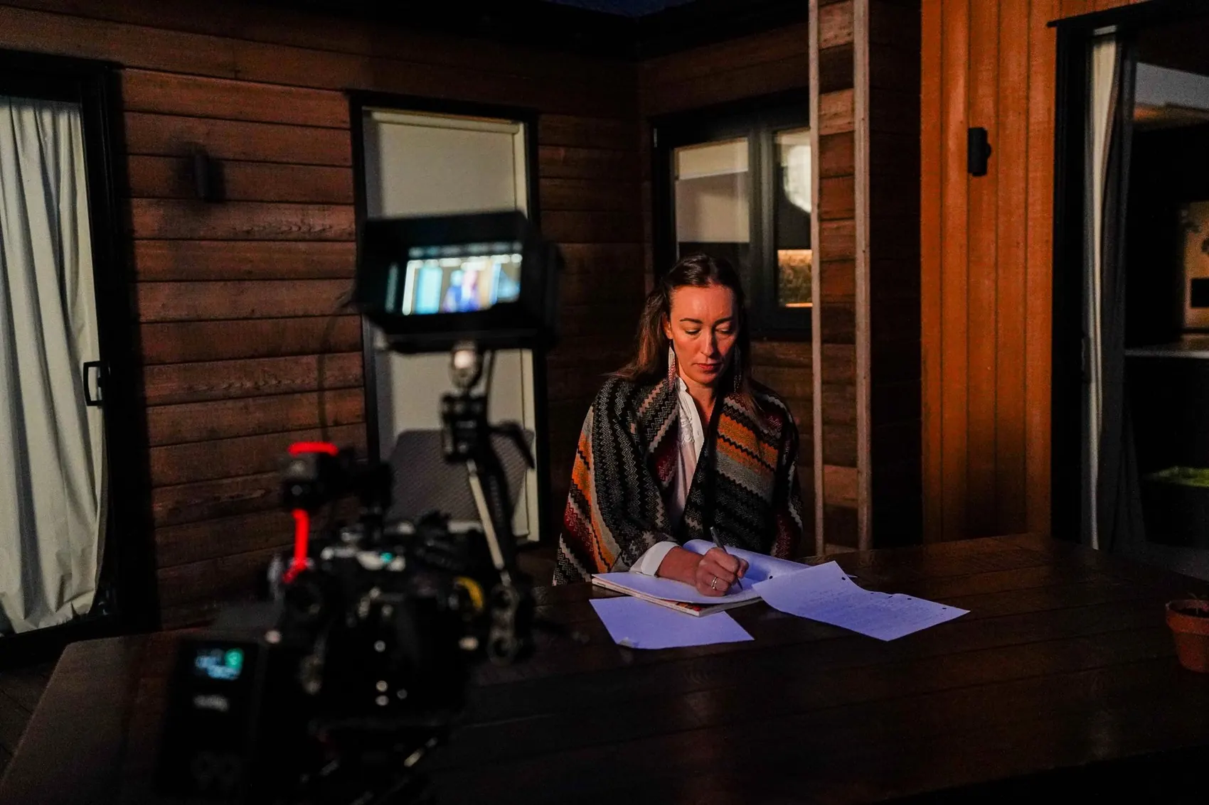 An actor reading at a table on the One In Ten set, with a cinema camera and monitor in the foreground