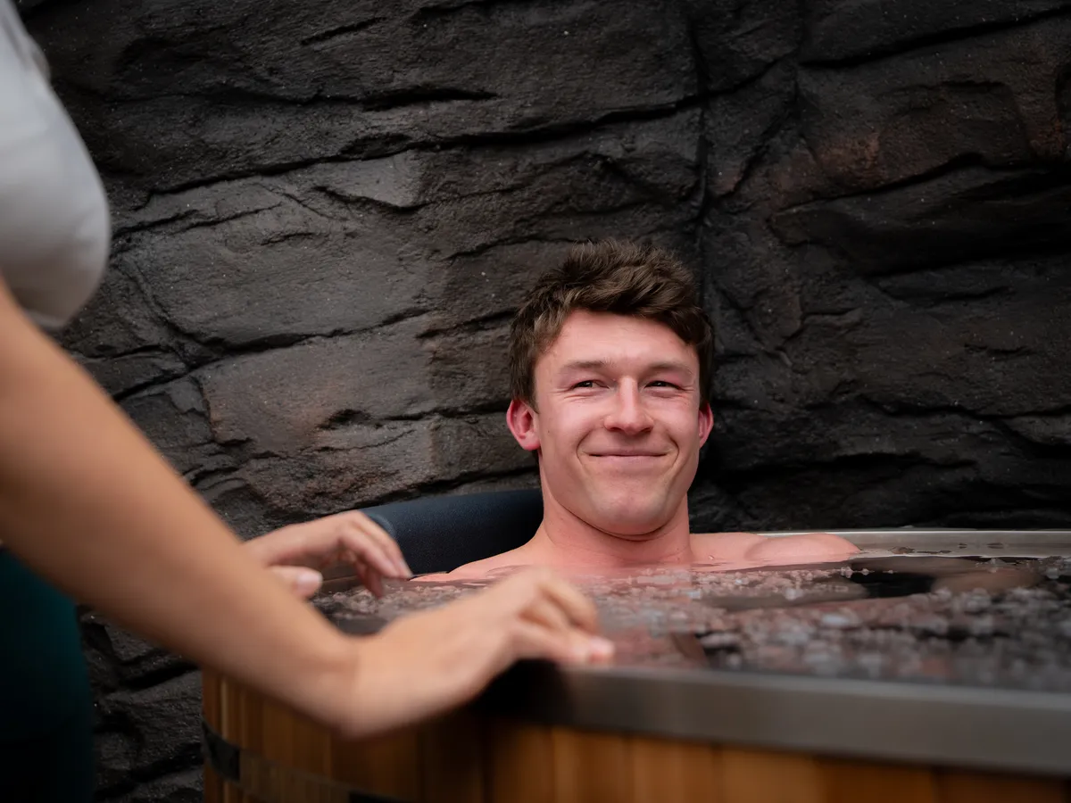 The model grinning in the ice bath as the trainer reaches over the rim