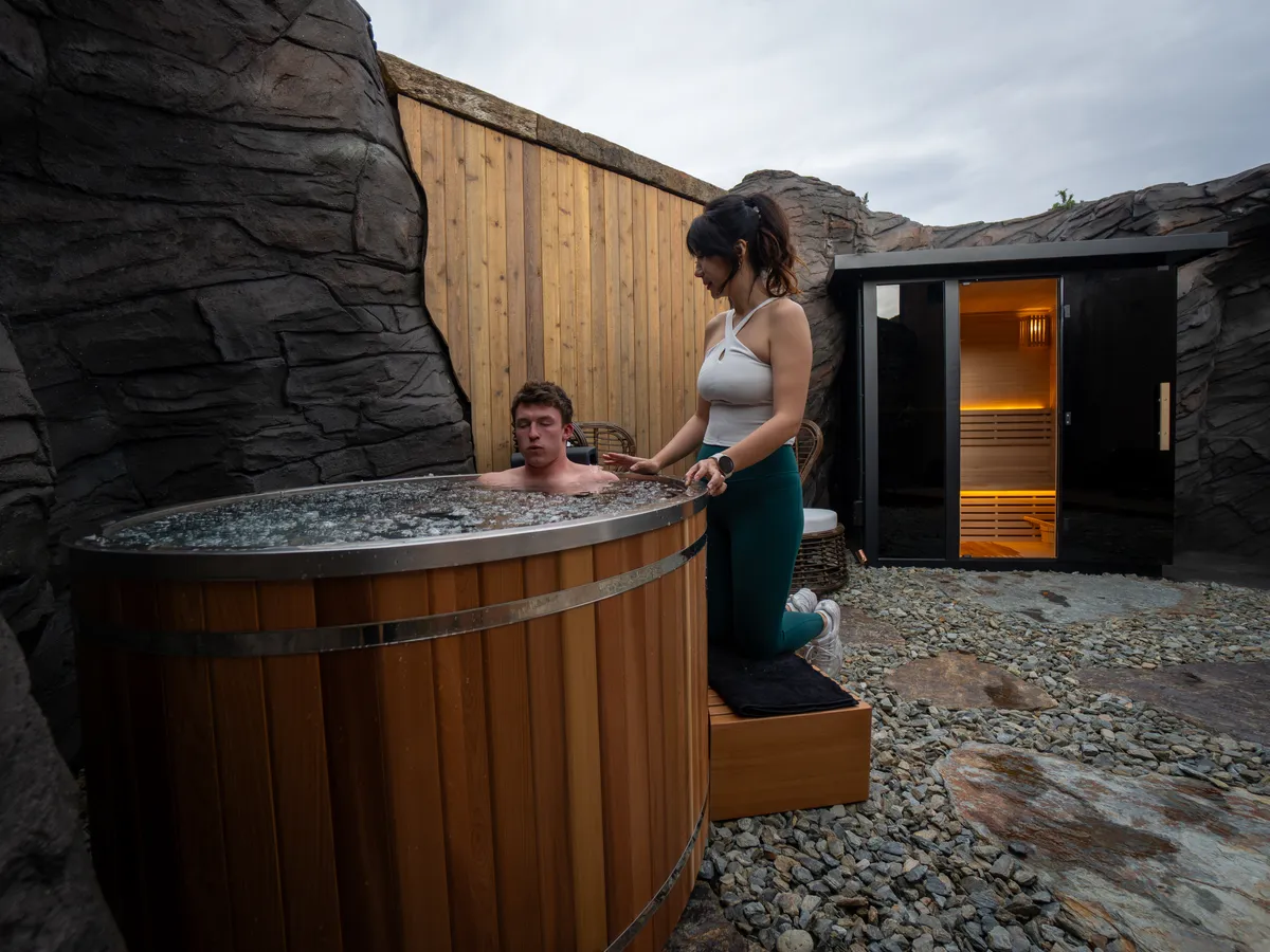 The ice bath in the Pure Senses courtyard, with the trainer standing beside the tub and the sauna cabin behind