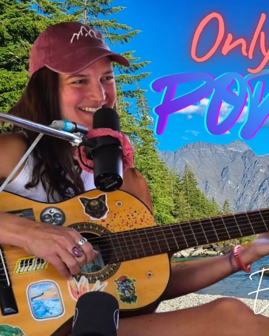 A musician with a guitar and microphone by Lake Wakatipu, from a Tuned In Trip episode